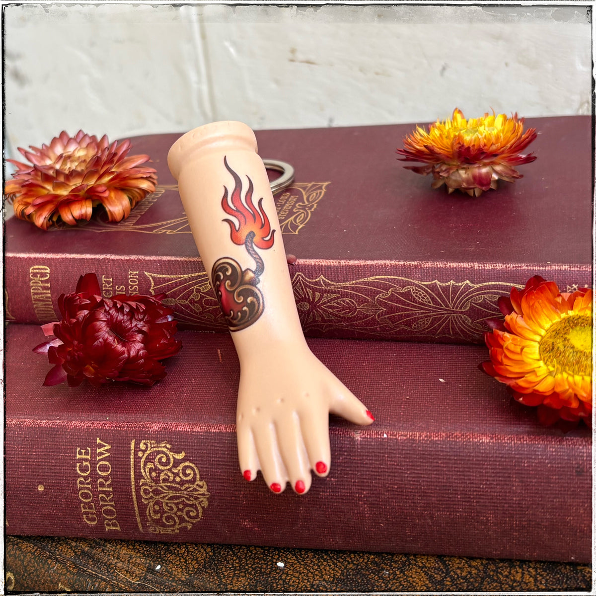 Porcelain Doll Arm Keyring Love Bomb

A recycled porcelain doll arm keychain with a tattoo of a love bomb and red fingernails, resting on stacked vintage red books with decorative flowers
